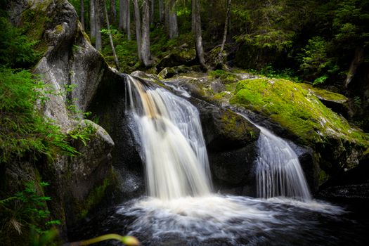 A tranquil waterfall flows over moss-covered rocks in a lush forest, capturing nature's serene beauty.