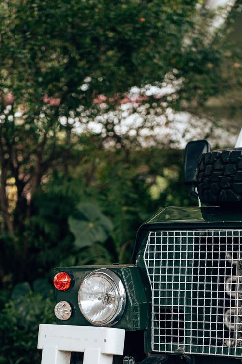 Free Detailed view of a classic vehicle's front headlight and grille, surrounded by greenery. Stock Photo