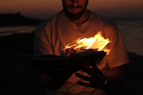 A Man in White Shirt Holding a Burning Book