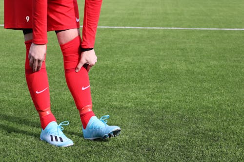 A Person Wearing Red Uniform and Red Socks with Blue Soccer Shoes