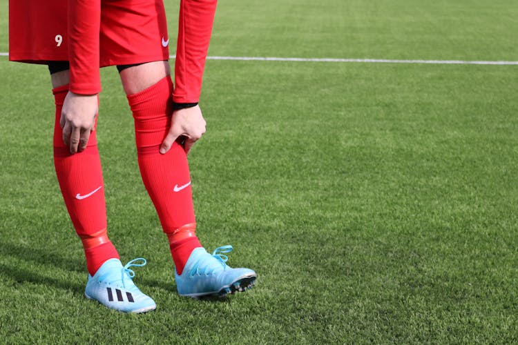 A Person Wearing Red Uniform And Red Socks With Blue Soccer Shoes