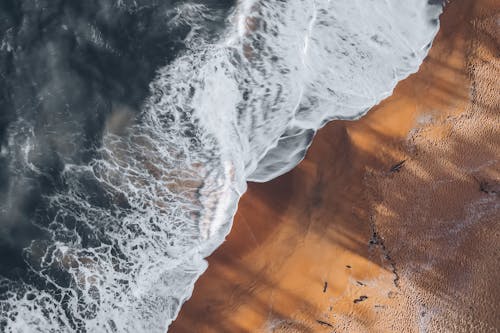 An Aerial Photography of Waves Crashing on Brown Sand