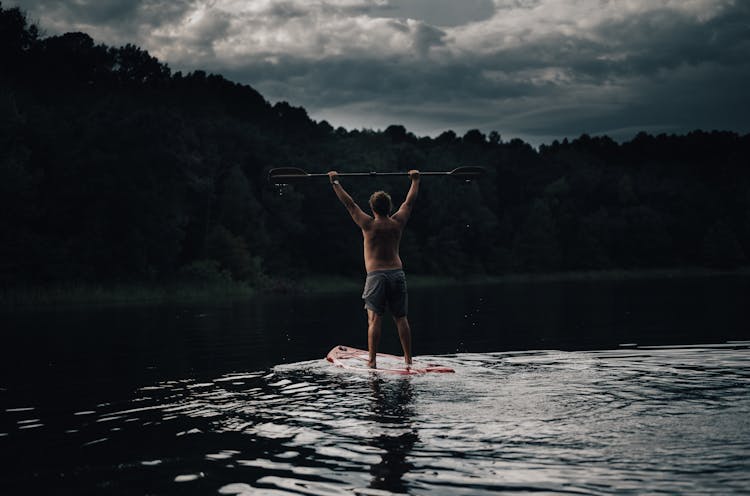 A Shirtless Man Standing On Paddle Board Holding A Paddle