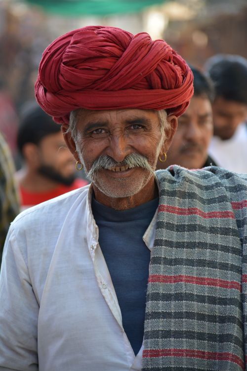 Free Portrait of an elderly Indian man with a red turban and white attire, smiling warmly outdoors. Stock Photo