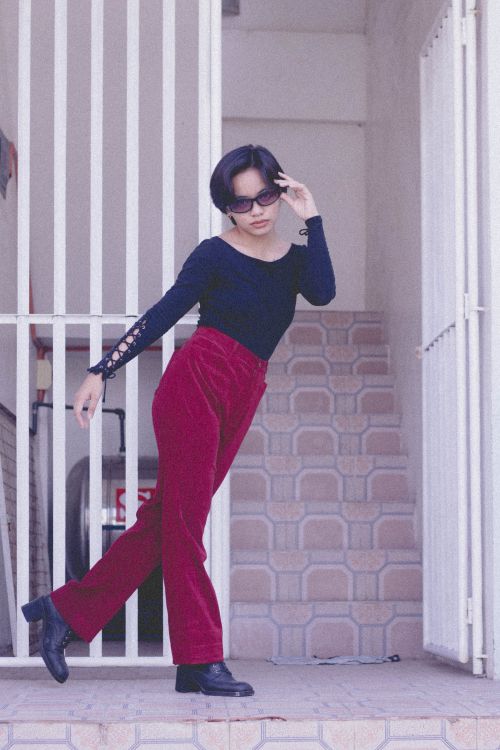 Free Fashion-forward woman in red pants and sunglasses posing stylishly by a metal gate. Modern aesthetic. Stock Photo