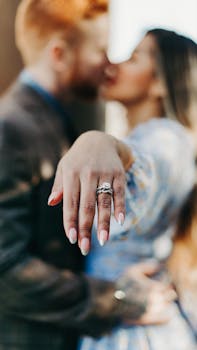 A couple embraces with focus on an elegant diamond engagement ring in the foreground.