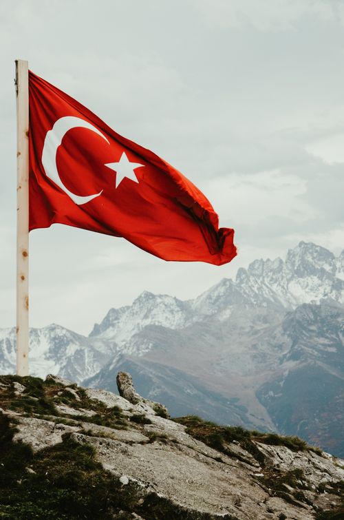 Free Turkish flag waving on a pole with majestic mountains in the background, captured during the day. Stock Photo