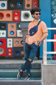 Fashionable man standing in front of a colorful speaker wall, exuding confidence and style.