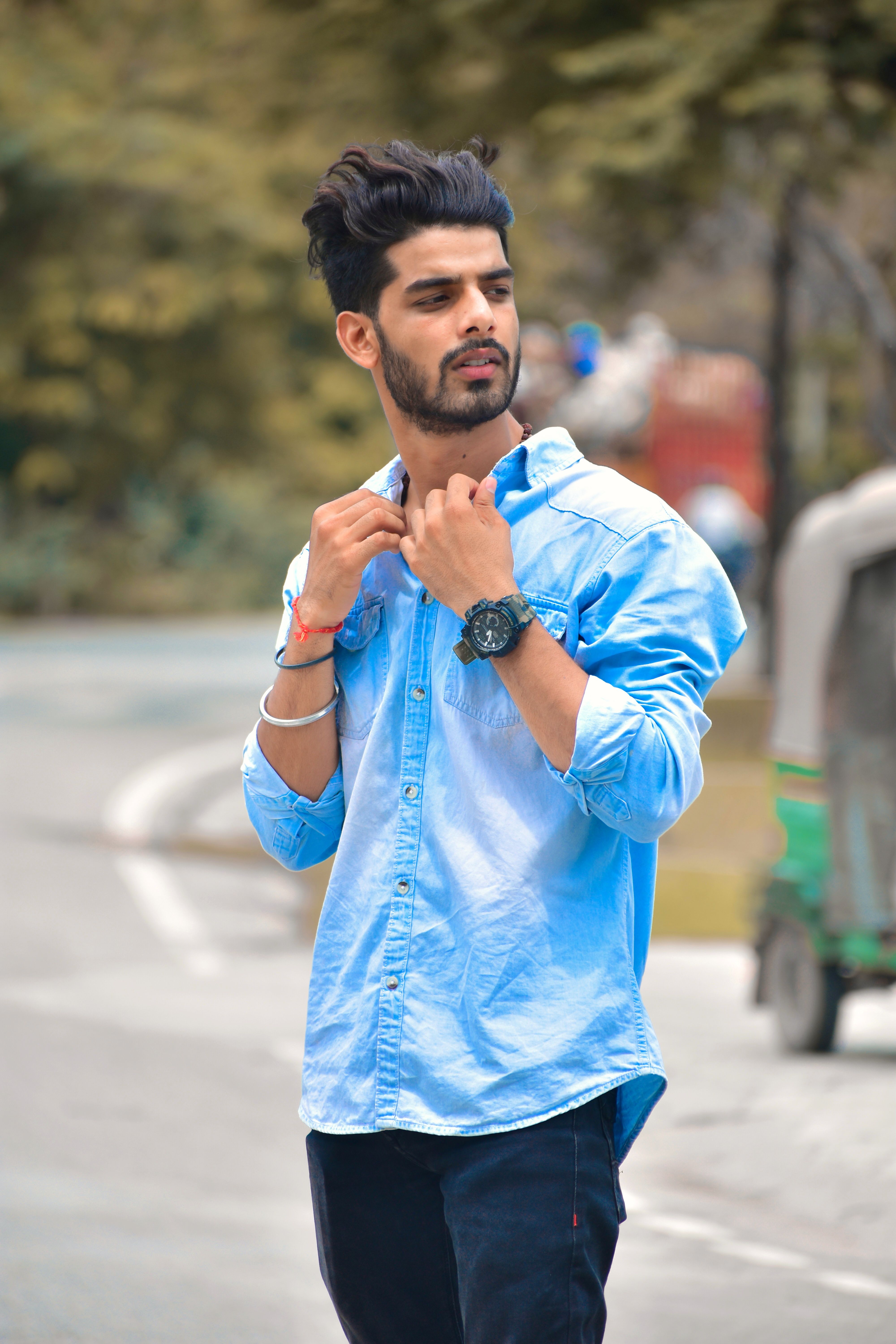 Portrait of a fashionable young man adjusting collar outdoors on a sunny day.