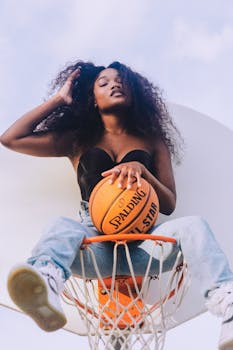A stylish portrait of a woman sitting creatively on a basketball hoop holding a Spalding ball in Orlando, FL.
