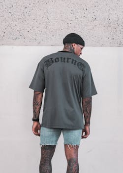 Stylish tattooed man in grey t-shirt and shorts, posing with urban flair.