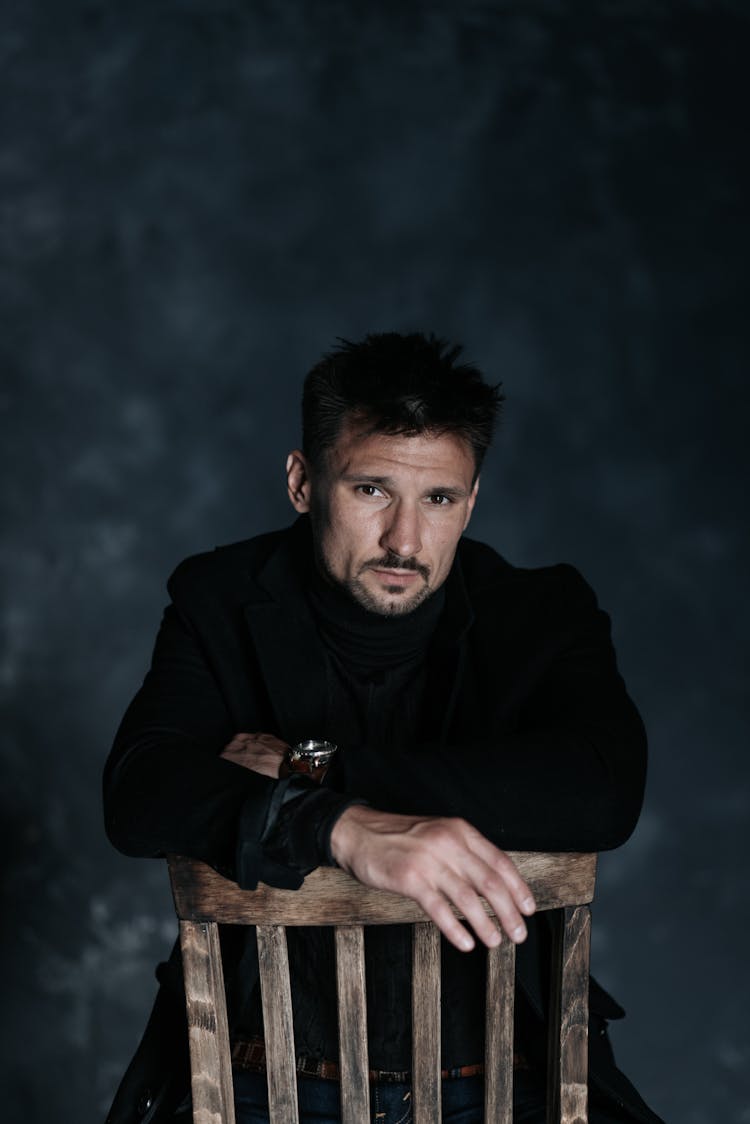 Man In Black Outfit Sitting On A Chair Backwards