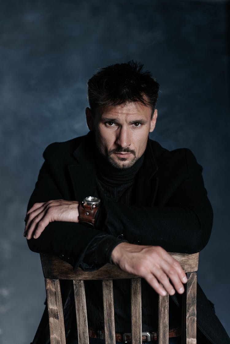 Man In Black Outfit Sitting On A Chair Backwards