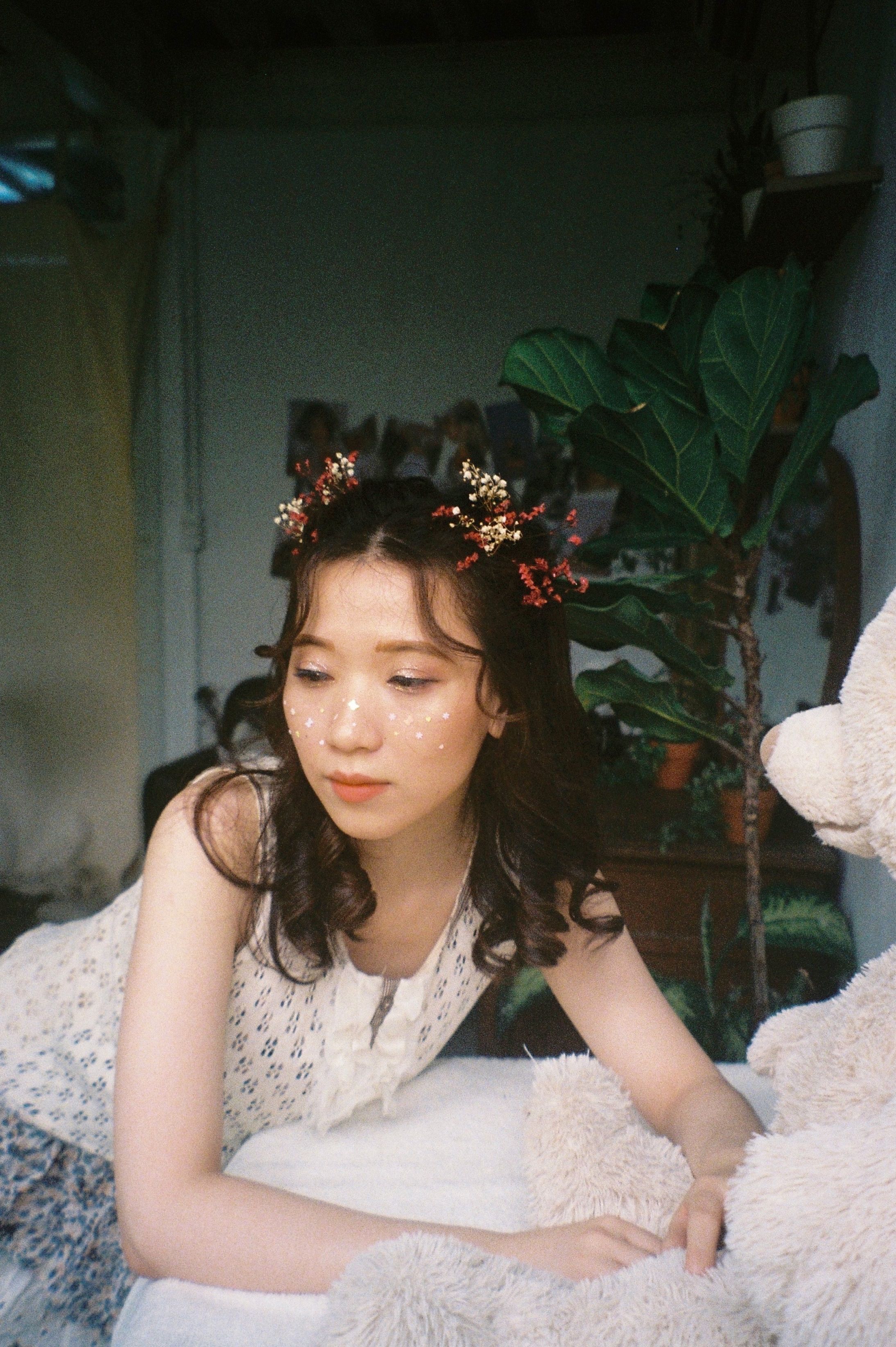 A young woman with floral accessories relaxing indoors with a teddy bear.