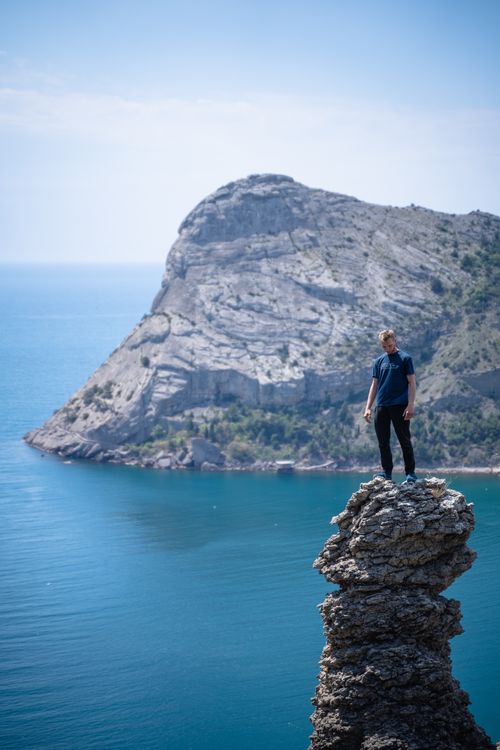 Free A man in a blue shirt stands on a rocky cliff with a view of the ocean below. Adventure awaits. Stock Photo