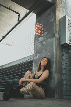 Model in fishnet stockings poses against concrete background in urban setting.