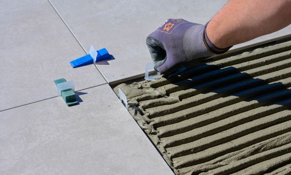 Tiling & Waterproofing โ Detailed view of gloved hand aligning tiles with levelers and spacers during construction.
