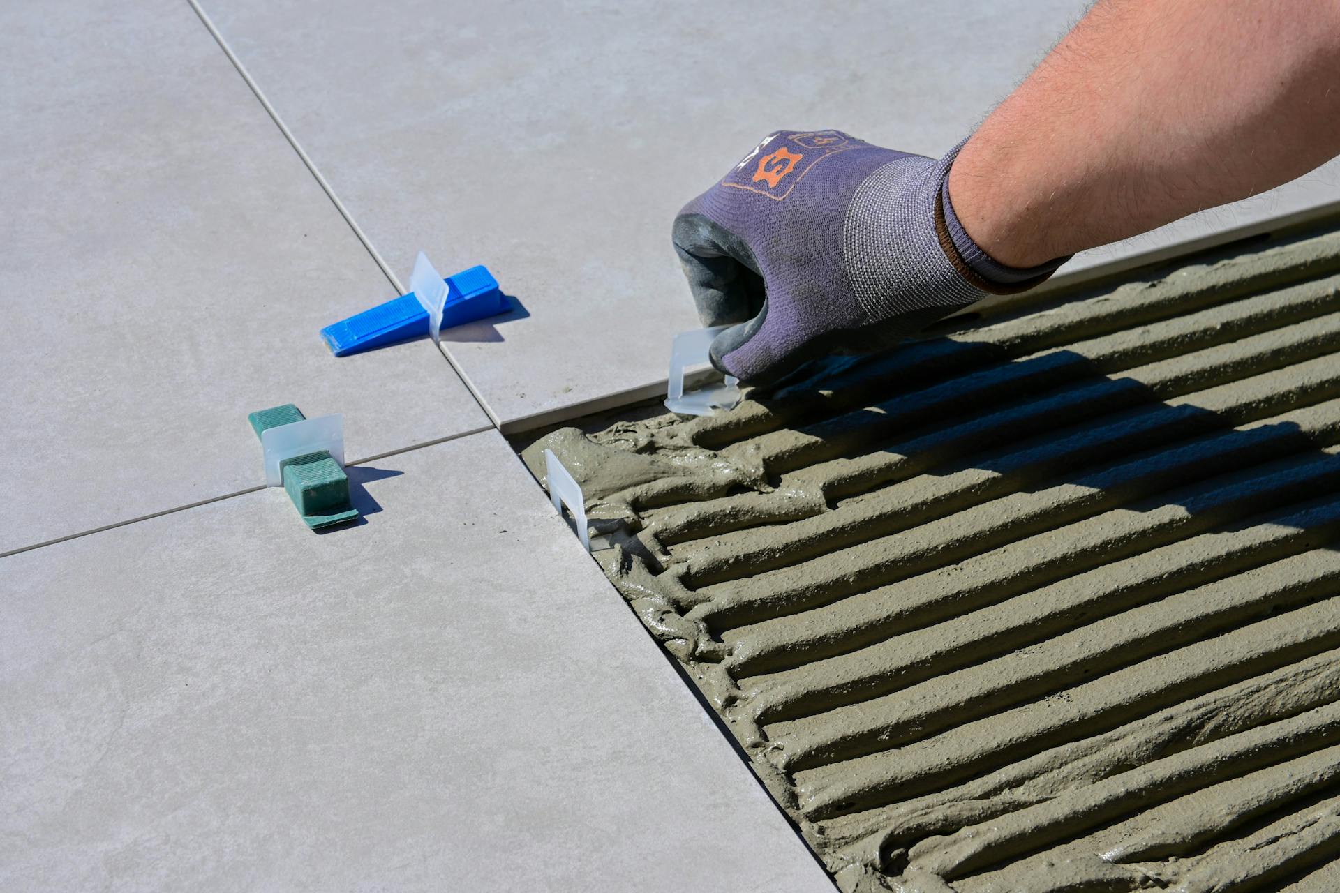 Detailed view of gloved hand aligning tiles with levelers and spacers during construction.