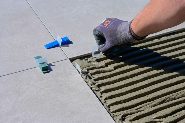 Installer laying polished marble flooring slabs with precision spacers