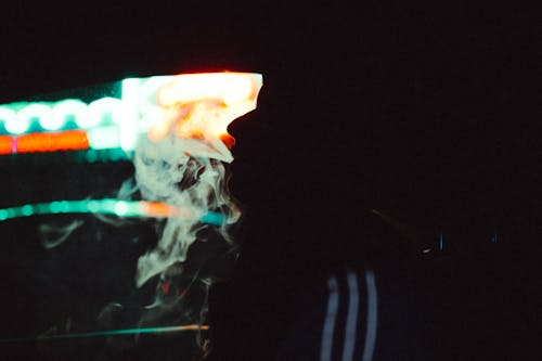 Silhouette of a Man Smoking on the Background of Neon Lights 