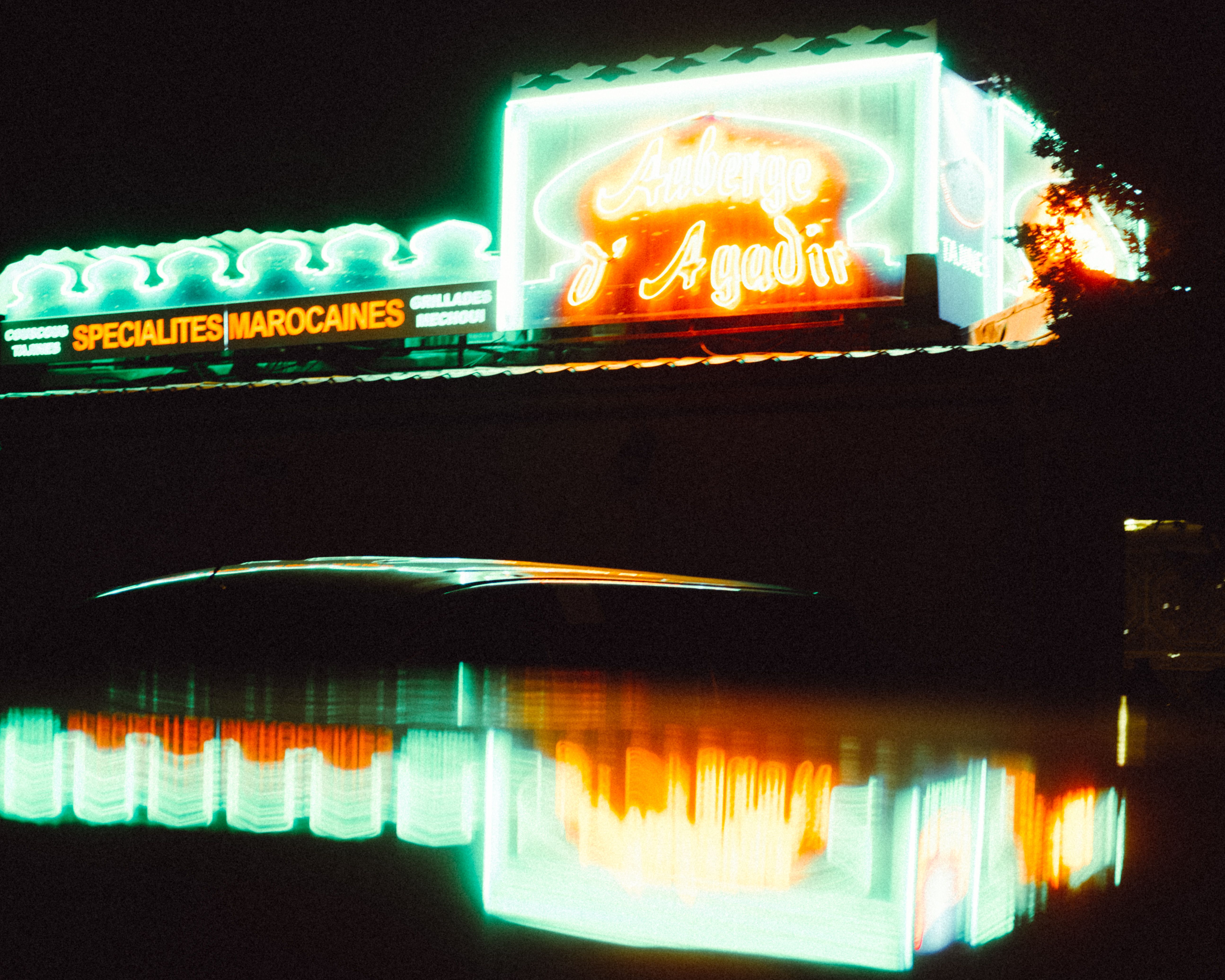 Colorful neon signs illuminate a night scene, reflecting vividly in water. A moody and urban atmosphere captured.
