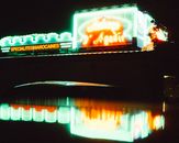 Colorful neon signs illuminate a night scene, reflecting vividly in water. A moody and urban atmosphere captured.