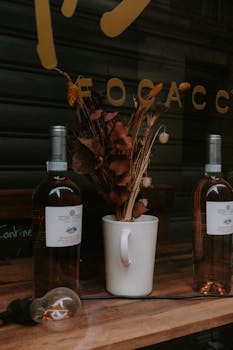 Two wine bottles and dried flowers in a mug on a rustic table, ideal for vintage settings.