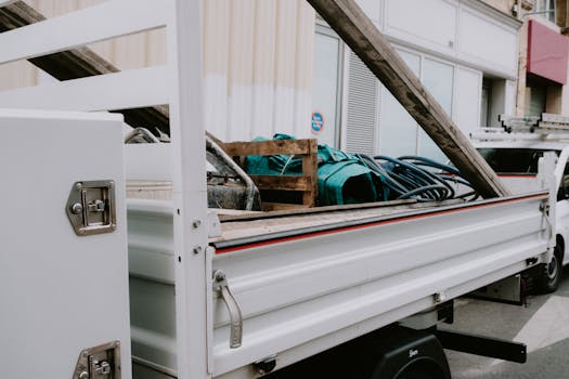A white construction truck loaded with building materials and equipment parked by a building.