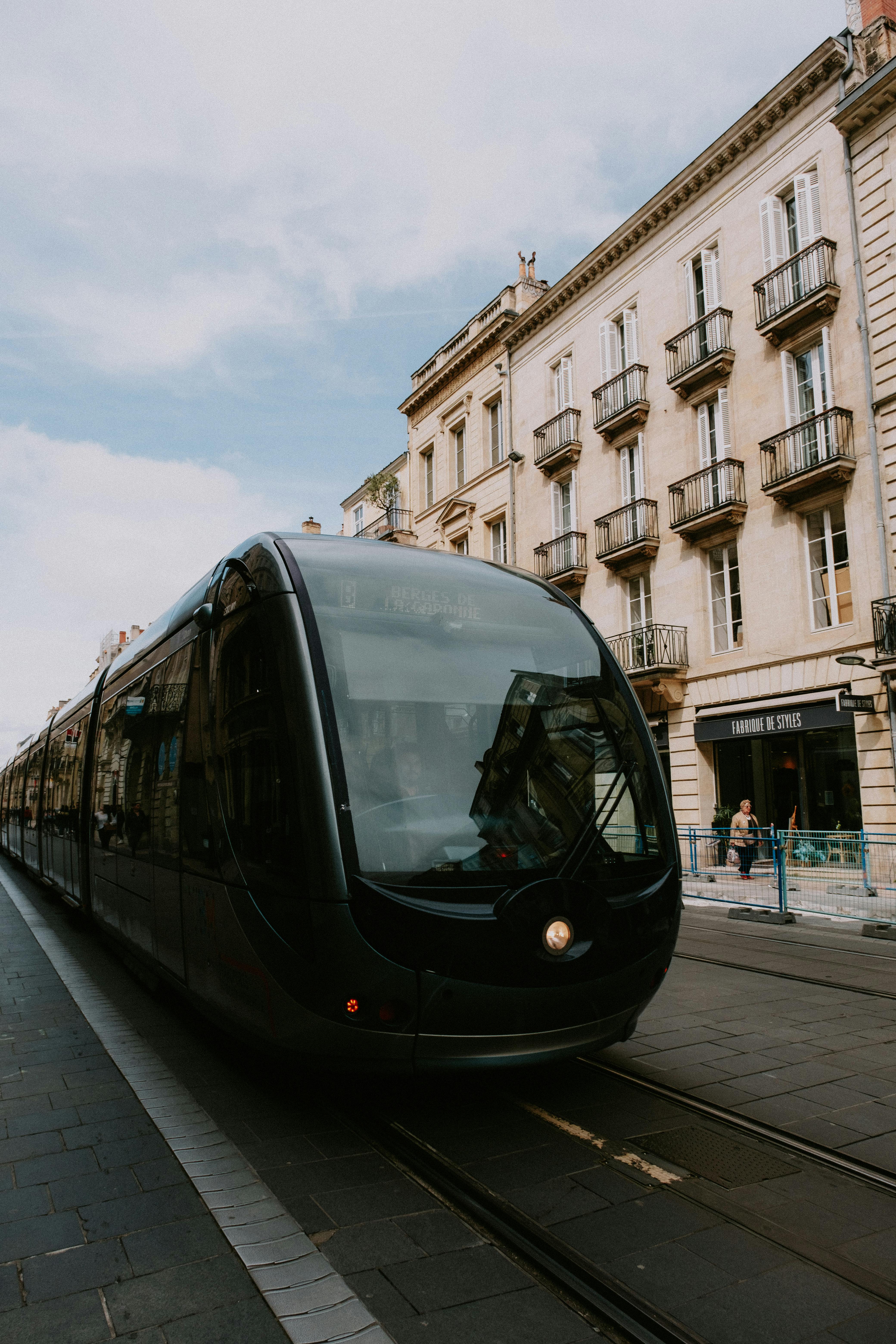 Free A sleek tram travels through an urban street lined with classic architecture under a clear sky. Stock Photo