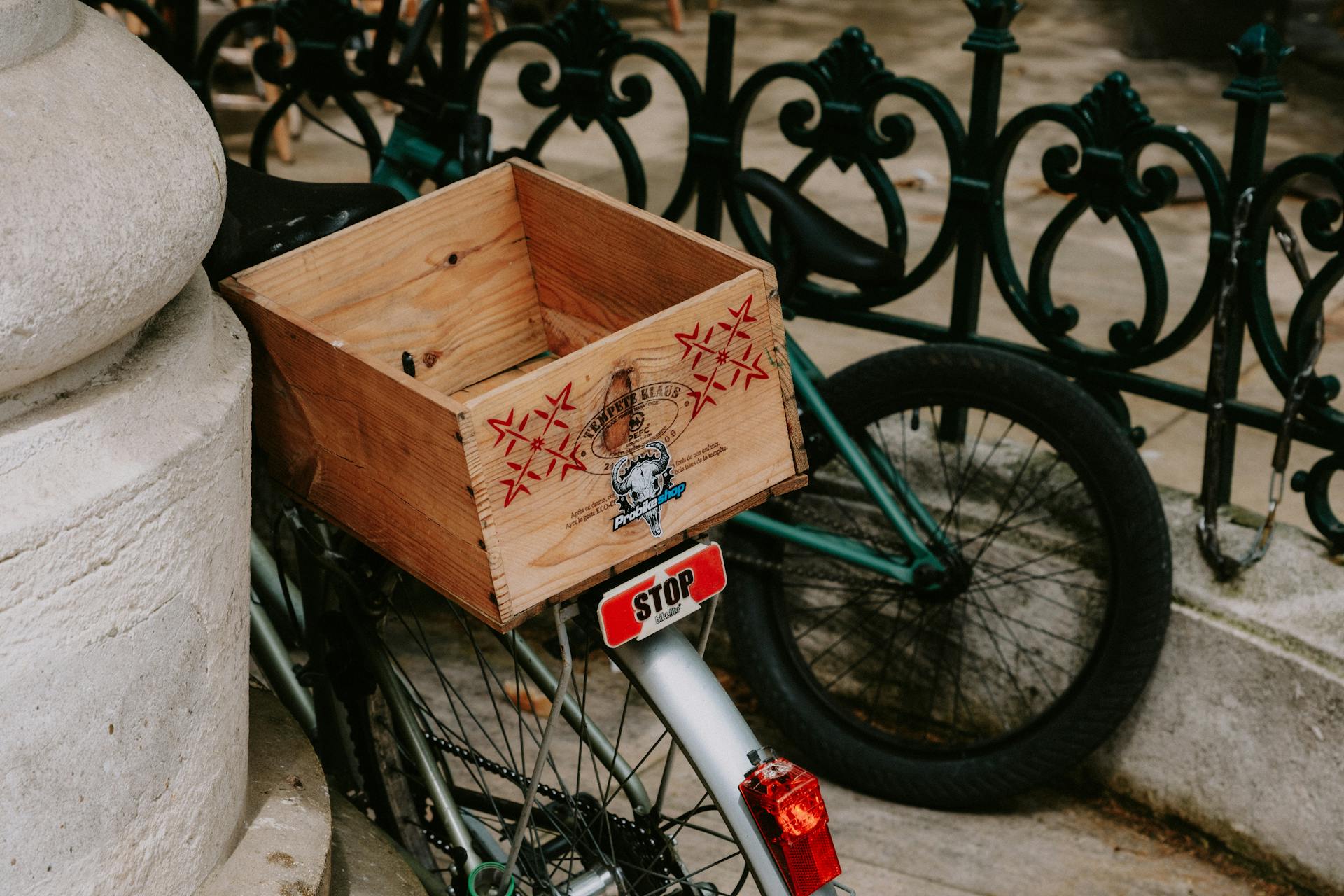 Retro bicycle with a wooden box parked against an ornate iron fence on a city street.