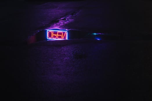 Dark urban street featuring a neon sign reflection on a rainy night pavement.