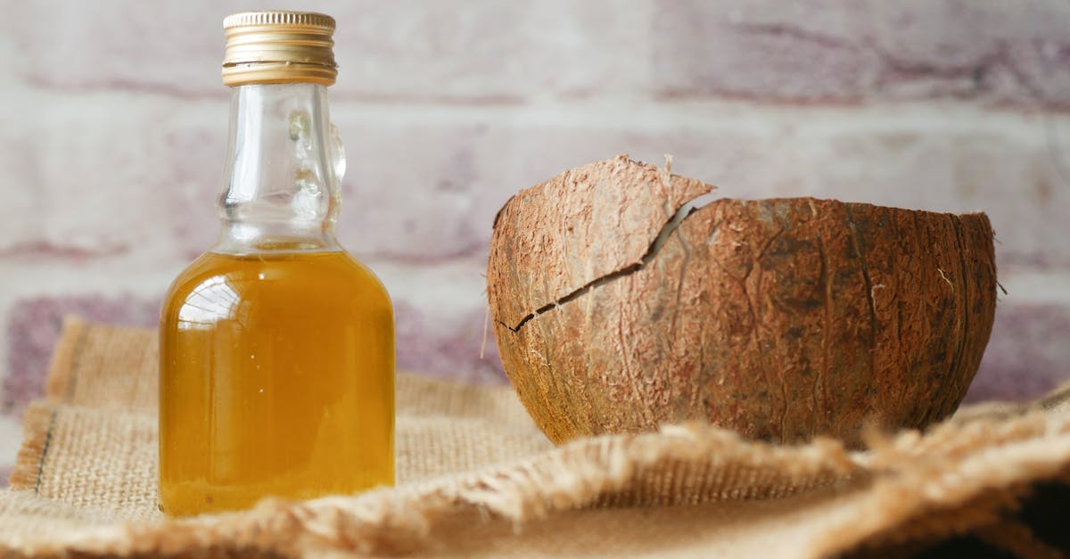 Bottle of coconut oil beside a cracked coconut shell on burlap fabric indoors. Bottle of coconut oil beside a cracked coconut shell on burlap fabric indoors.