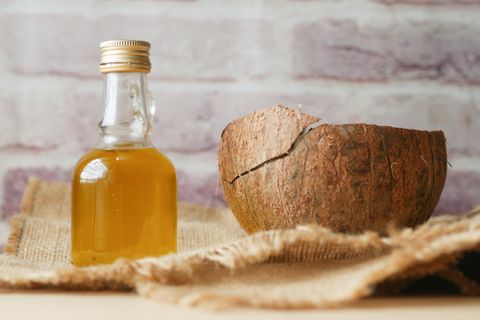 Glass bottle of coconut oil beside a cracked coconut