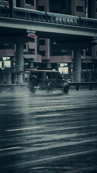 Luxury SUV driving on a wet road in Dubai under a modern urban bridge.
