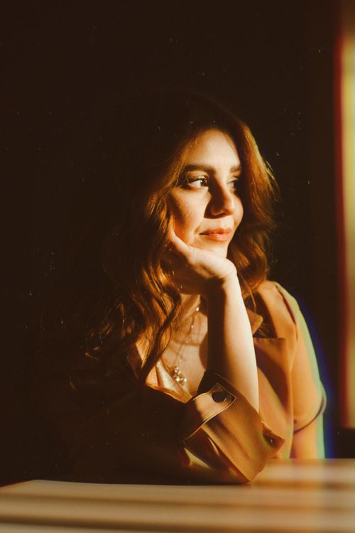 Free Portrait of a woman in warm light, hand on chin, pensive expression indoors. Stock Photo