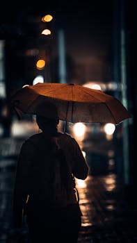 A solitary woman walks through a rainy street in Dubai at night, illuminated by city lights.