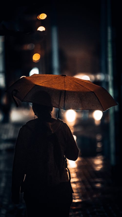 Free A solitary woman walks through a rainy street in Dubai at night, illuminated by city lights. Stock Photo