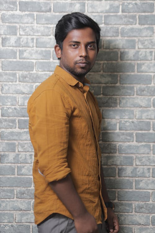 Man in Brown Long Sleeves Standing Beside a Brick Wall