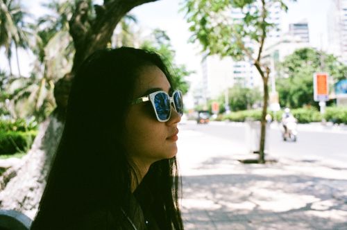 Free Profile of a woman wearing sunglasses enjoying a sunny day in a city park. Stock Photo