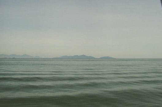 Calm ocean waves under a cloudy sky with distant islands in view.