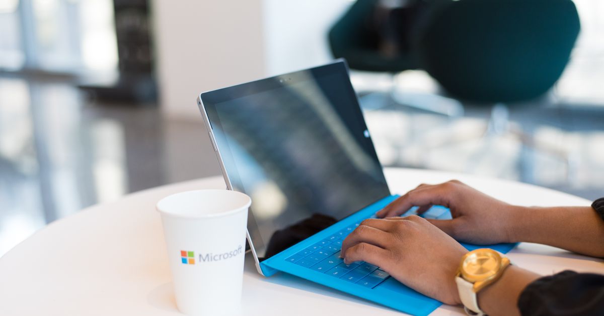 Hands typing on a blue keyboard with a branded cup on a table.