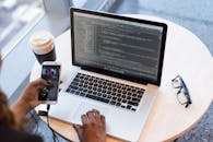 程序员在笔记本电脑上管理代码，同时用智能手机处理多项任务，展现了现代科技工作空间的特点