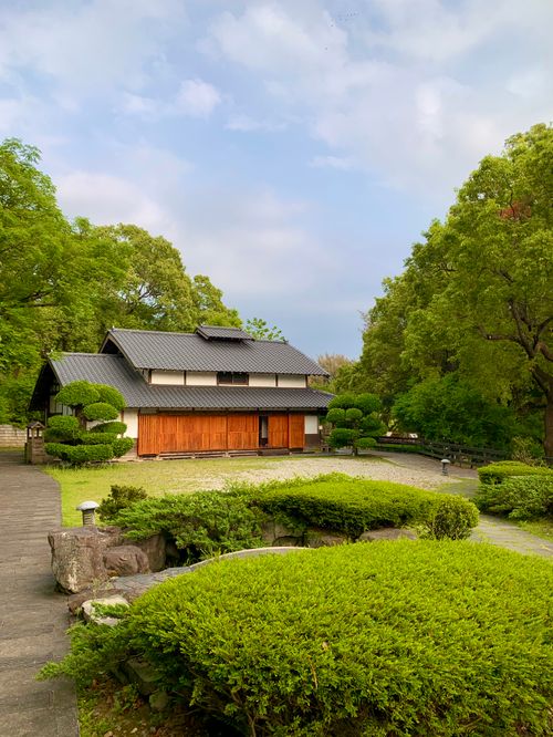 Free Serene view of a traditional Japanese house surrounded by a lush, green garden under a clear sky. Stock Photo