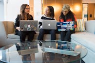 在现代办公环境中，三名女性正使用笔记本电脑进行工作讨论