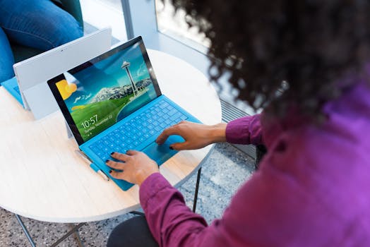 A woman with curly hair works on a laptop indoors with a Seattle skyline on screen.