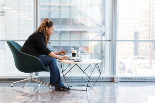 Free Business woman using smartphone and laptop in a bright, modern office space. Ideal for technology and work themes. Stock Photo