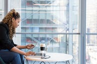 一位女士在室内用智能手机操作笔记本电脑工作，展现了现代远程办公的场景