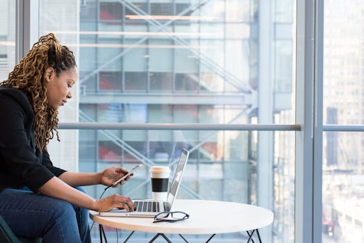 一位女士在室内用智能手机操作笔记本电脑工作，展现了现代远程办公的场景