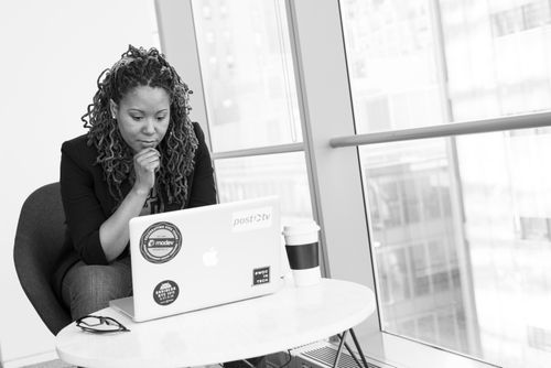 Free Woman sitting at laptop, focused on remote work. Black and white aesthetic indoors. Stock Photo
