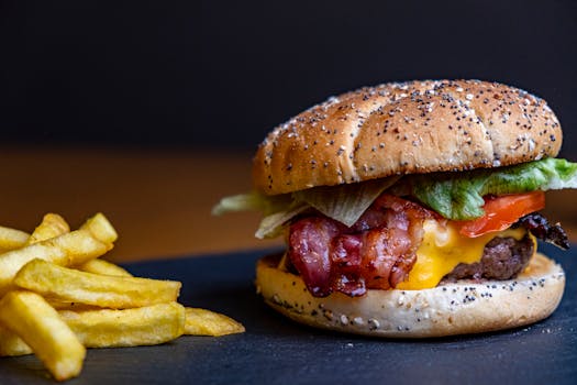 Close-up of a juicy cheeseburger with crispy fries on a black surface.